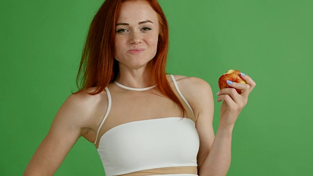 美丽的女运动员吃一个苹果在绿色的背景视频素材