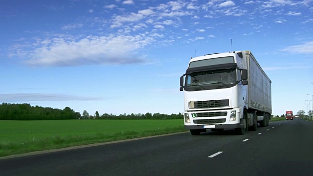 高速行驶的白色半挂车与货物拖车行驶在公路两旁的田地。视频下载