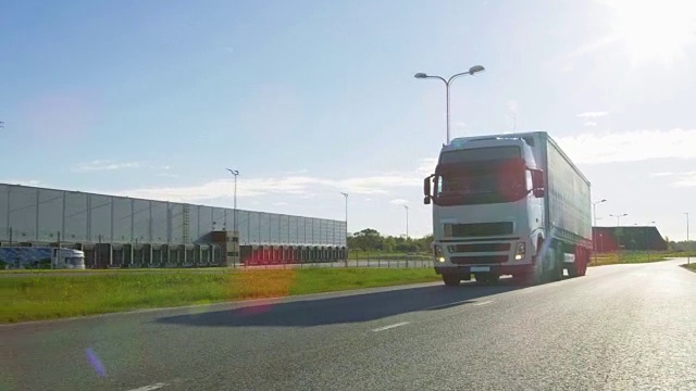 白色半挂车与货物拖车在空旷的道路上。工业仓库旁的高速公路和阳光普照。视频下载
