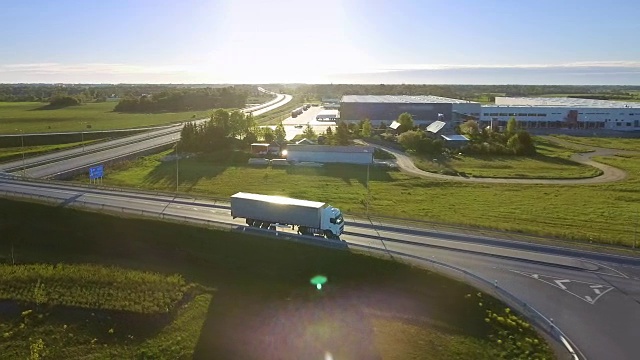 带货运拖车的白色半挂车通过高速公路立交桥鸟瞰图。十八惠勒是新的，装载仓库在背景中看到。视频素材