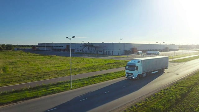空中跟踪拍摄的白色卡车与半挂车连接移动通过工业仓库，农村地区。日落。视频素材