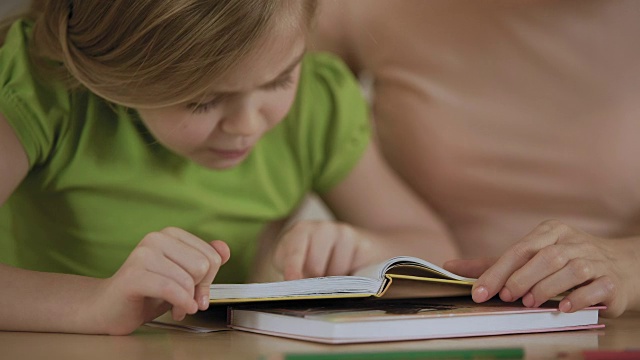 聪明的小女孩专注地读着书里有趣的故事，笑着对妈妈说视频素材