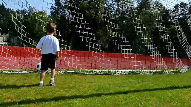 一个3岁小男孩在足球场上进球的跟踪摄像机视频素材