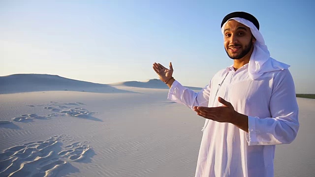一个阿拉伯人站在广阔的沙漠中，在夏日的空旷中，看着镜头告诉我们信息，和我们握手视频素材