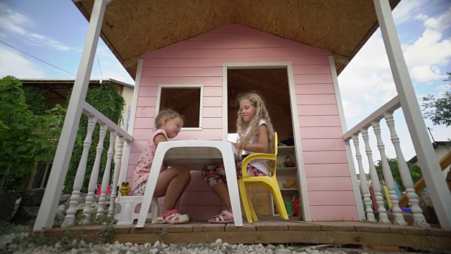 孩子们在一个粉红色木制玩具屋的阳台上玩得很开心视频素材