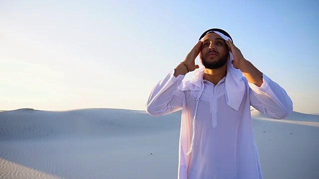穆斯林男子感到头痛和全身不适，忍受在温暖的夏天站在沙漠中间视频下载