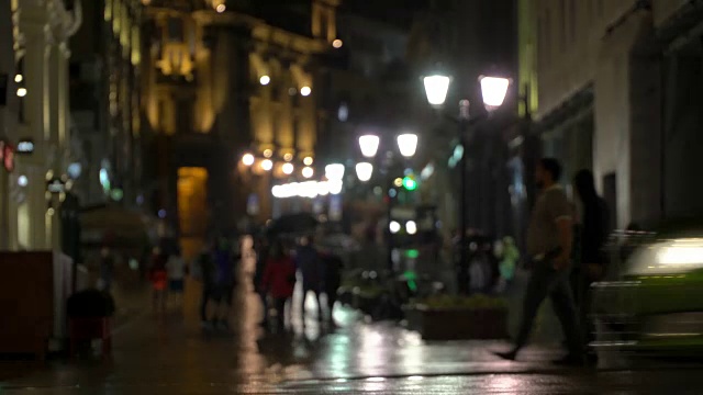 在雨夜的城市里，街道上挂满了路灯，柏油从雨中闪闪发光。不认识的行人，年轻人。现代都市夜生活的概念生活方式。汽车和行人视频素材