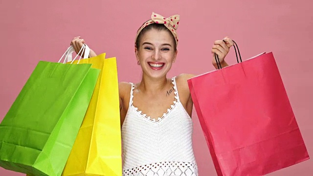 年轻的白人妇女看着相机拿着购物袋在粉红色的背景高兴因为销售。视频素材