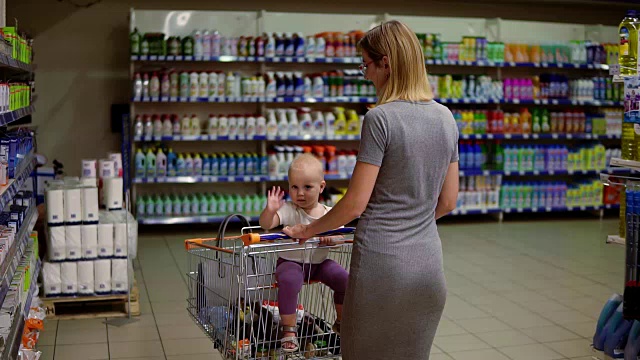 一位年轻的母亲带着她的小婴儿在超市里走着。那孩子环顾四周，挥着手视频素材