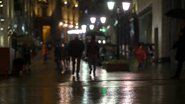 在雨夜的城市里，街道上挂满了路灯，柏油从雨中闪闪发光。不认识的行人，年轻人。现代都市夜生活的概念生活方式。汽车和行人视频素材