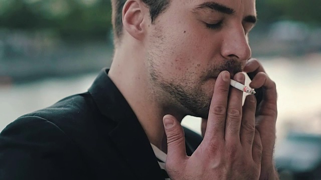年轻人一边抽烟一边用智能手机。男人用手机打电话视频素材