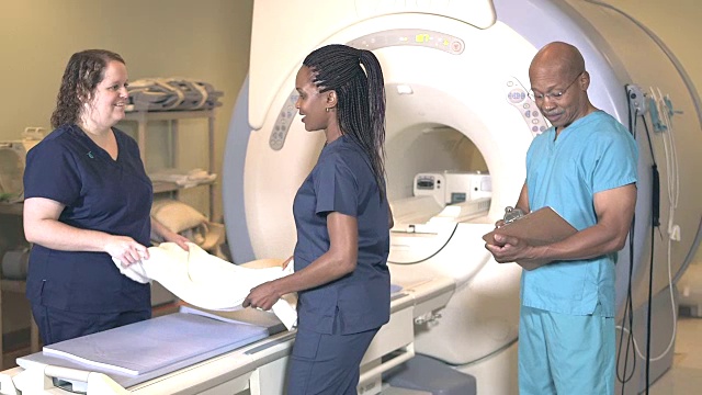 三名医学专业人员在核磁共振扫描仪室工作视频素材