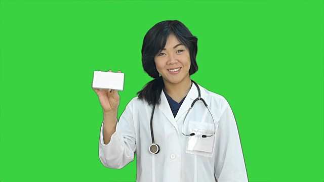 亚洲女医生展示一瓶药片看着摄像头在绿色屏幕上，色度键视频下载