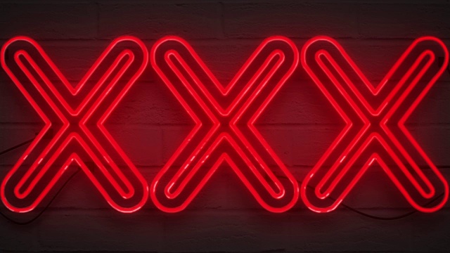 闪烁闪烁的红色霓虹灯招牌在砖墙的背景下，性感的成人表演夜总会XXX招牌视频下载