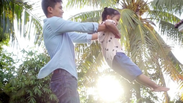 亚洲父亲与幸福的女儿围绕在花园，慢镜头拍摄在光的自然视频购买