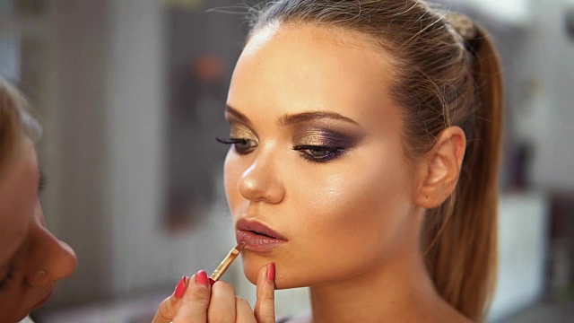 特写的专业化妆师使用特殊的画笔涂抹口红高加索模型。在嘴唇上涂唇彩。专业化妆视频素材