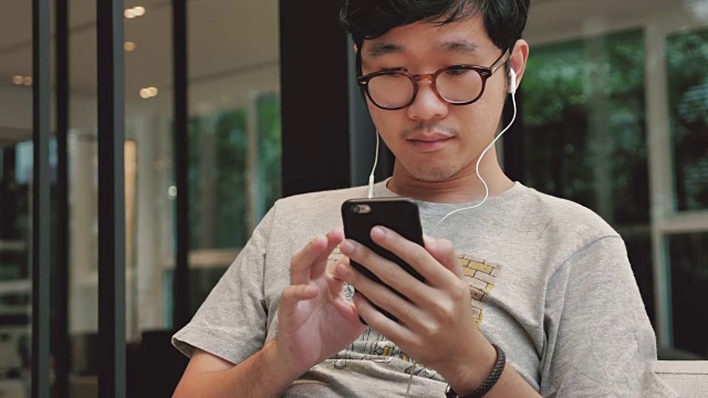亚洲男人在智能手机上选择和听音乐，4K视频下载