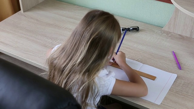 小女孩在笔记本上用尺子用铅笔画线。回到学校的概念。年轻女孩坐在屋里的桌子旁。浅色木桌白种人女孩。钢笔玻璃杯放在桌子上。视频素材