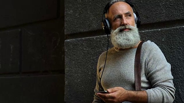 一个留着胡子的人一边听音乐一边看手机视频素材