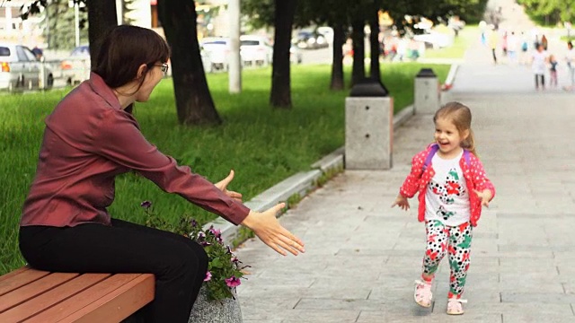 一个小女孩跑向坐在长凳上的妈妈。视频素材