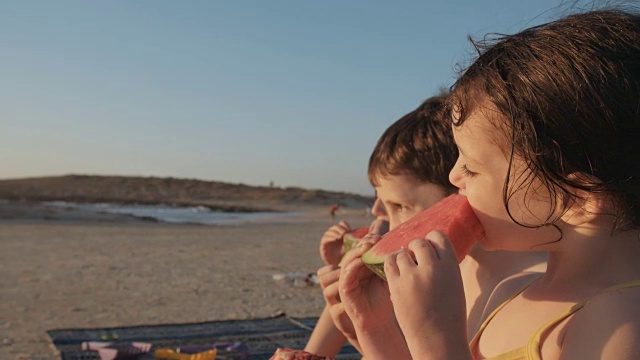 三个孩子在海滩上吃西瓜视频素材
