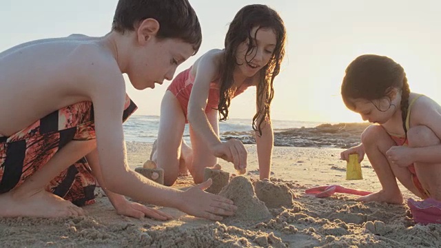 三个孩子在沙滩上玩，一起建沙堡视频素材