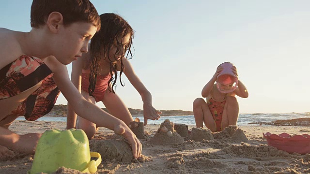 三个孩子在沙滩上玩，一起建沙堡视频素材