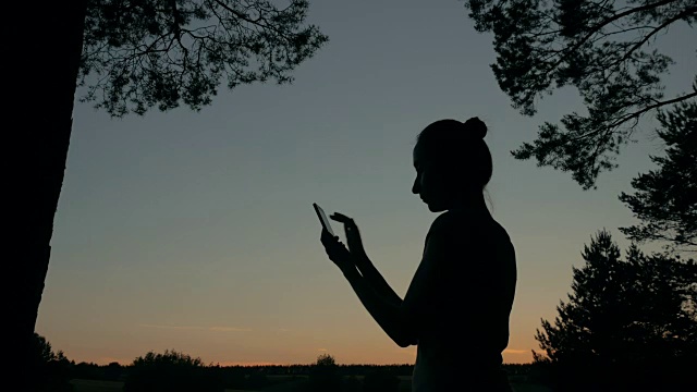 日落后，一名女子在森林里使用智能手机视频素材
