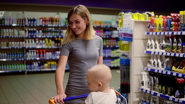 一位年轻的母亲带着她的孩子坐在超市的购物车里，推着购物车在不同的部门之间来回走动，选择产品视频素材