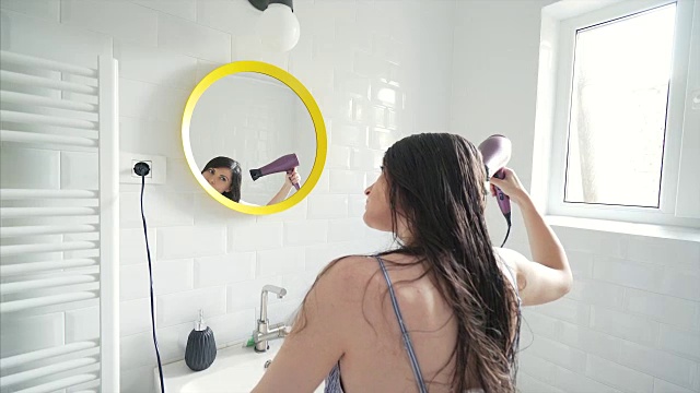 一个年轻女子在浴室里晾干头发。视频素材