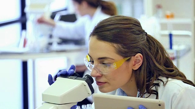 女科学家在实验室中使用数字平板和显微镜视频下载