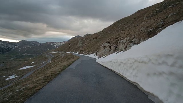 在秋天阴云密布的傍晚，汽车沿着山路行驶在户外的左边山谷，右边是密实的积雪视频素材