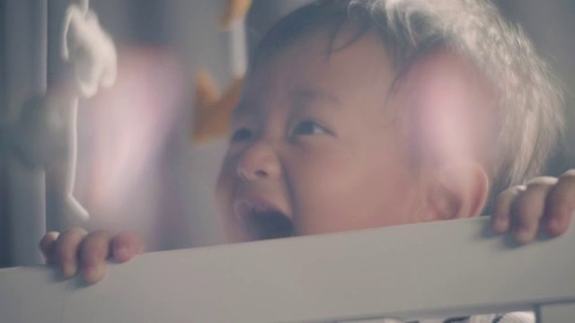 小男孩站在家里的婴儿床里大笑。视频下载