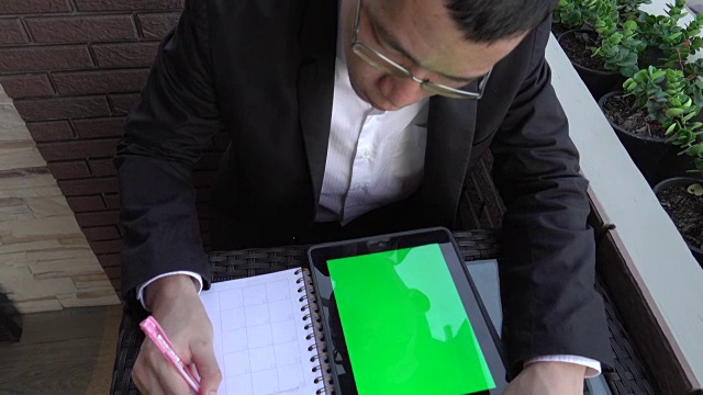 4k:商人肩拍使用平板电脑绿色屏幕写笔记视频素材