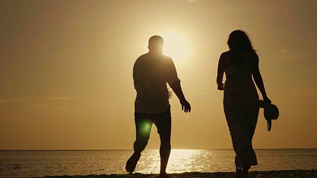 情感上享受海边的假期。一对年轻的夫妇在大海和夕阳的背景下愉快地拥抱着视频素材