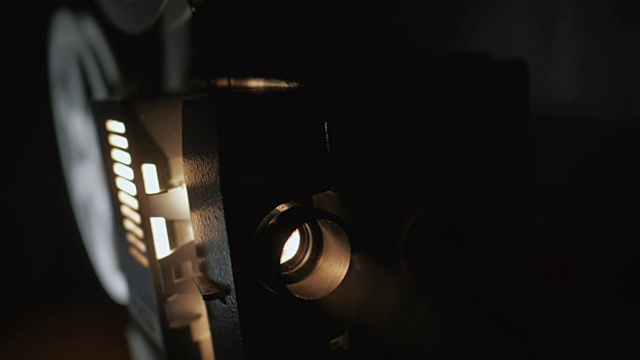 老式老式的超级8毫米电影放映机的正面，光线投射在黑暗的房间旁边的一堆散开的胶卷。老式剧院聚光灯在黑色窗帘与灰尘漂浮视频素材