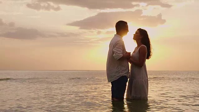 日落时分，一对相爱的年轻情侣站在海边。互相看着对方视频素材