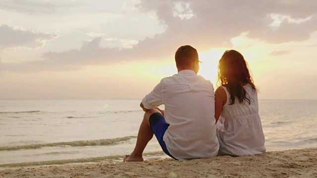 一男一女并排坐在沙滩上。他们一起看着海面上的日落视频素材