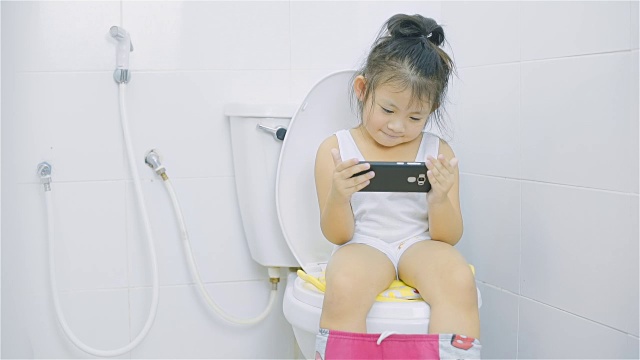 看智能手机的小女孩坐在厕所的马桶上视频购买
