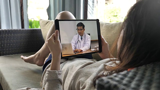 一名病人躺在沙发上，用平板电脑与医生视频交谈视频下载