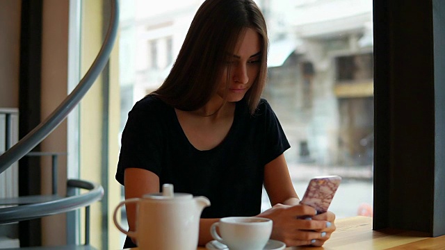 迷人的年轻女士与自然化妆使用她的手机在咖啡店。现代设备的使用。网上购物，积极的生活方式视频素材