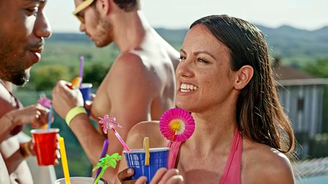 一个穿着泳衣，手里拿着一杯鸡尾酒的女人在泳池边和一个男人笑着说话视频素材