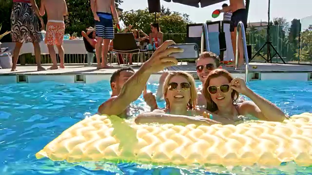 四个朋友在阳光下的泳池里自拍视频素材