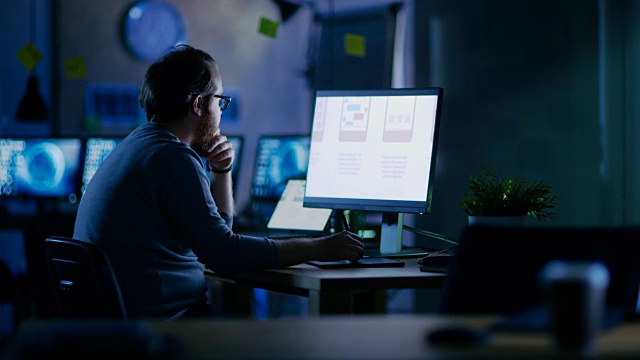 男性移动应用程序开发人员在他的个人电脑上使用两个显示器的图形。他在一间空办公室里工作到深夜。视频素材