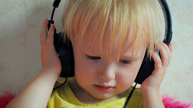 一个两岁的小女孩坐在沙发上，戴着耳机听音乐视频素材