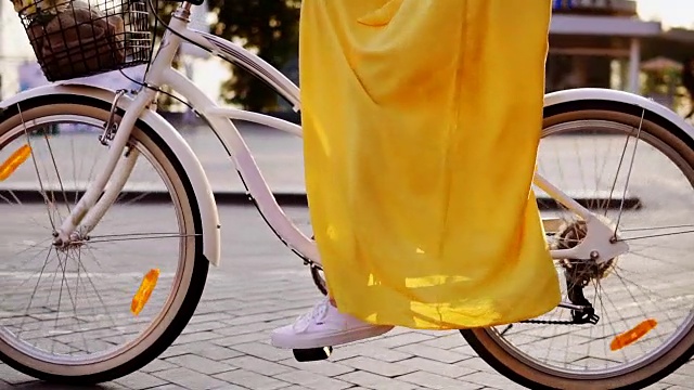 一个白色城市自行车的轮子旋转的特写。有铃铛，篮子和花的城市自行车。清晨，一个面目全非的女人骑着一辆城市自行车。替身。Slowmotion视频素材