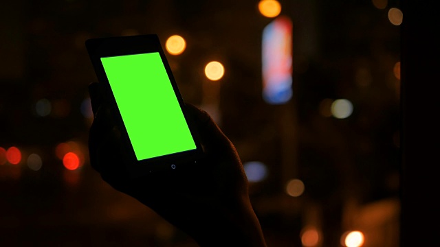 一个女人在看绿色屏幕的智能手机视频下载