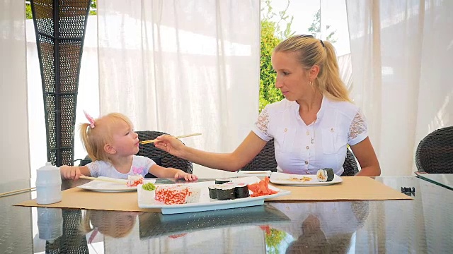 妈妈和女儿在一个夏日户外餐厅用筷子吃寿司。视频素材