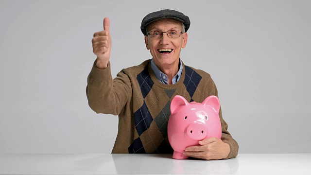 快乐的老人拿着存钱罐，竖起大拇指视频下载