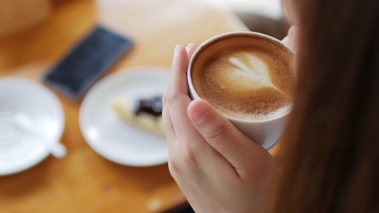 一个女人在咖啡厅拿咖啡拿铁艺术，摄影车从左到右拍摄视频下载